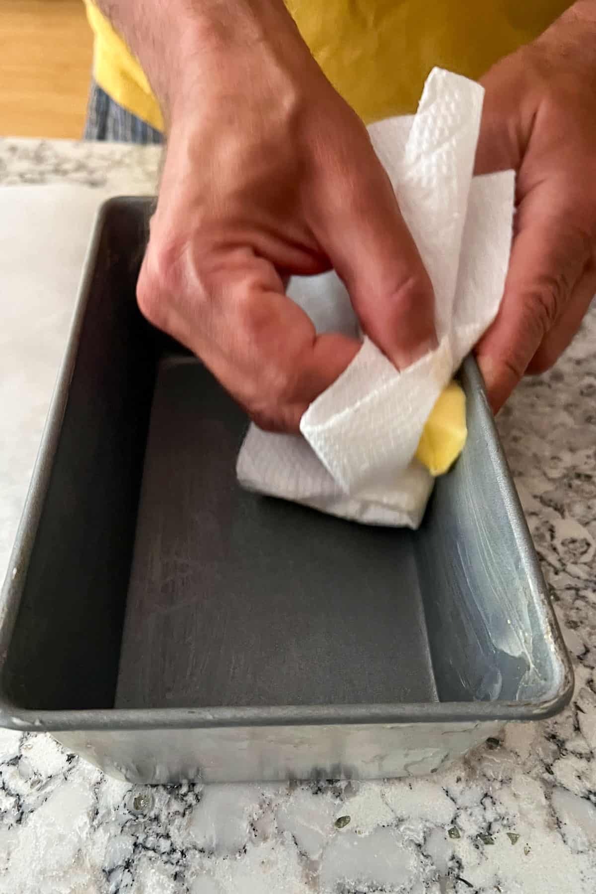 hand holding a blob of butter with a paper towel and rubbing it on the inside of a loaf pan.