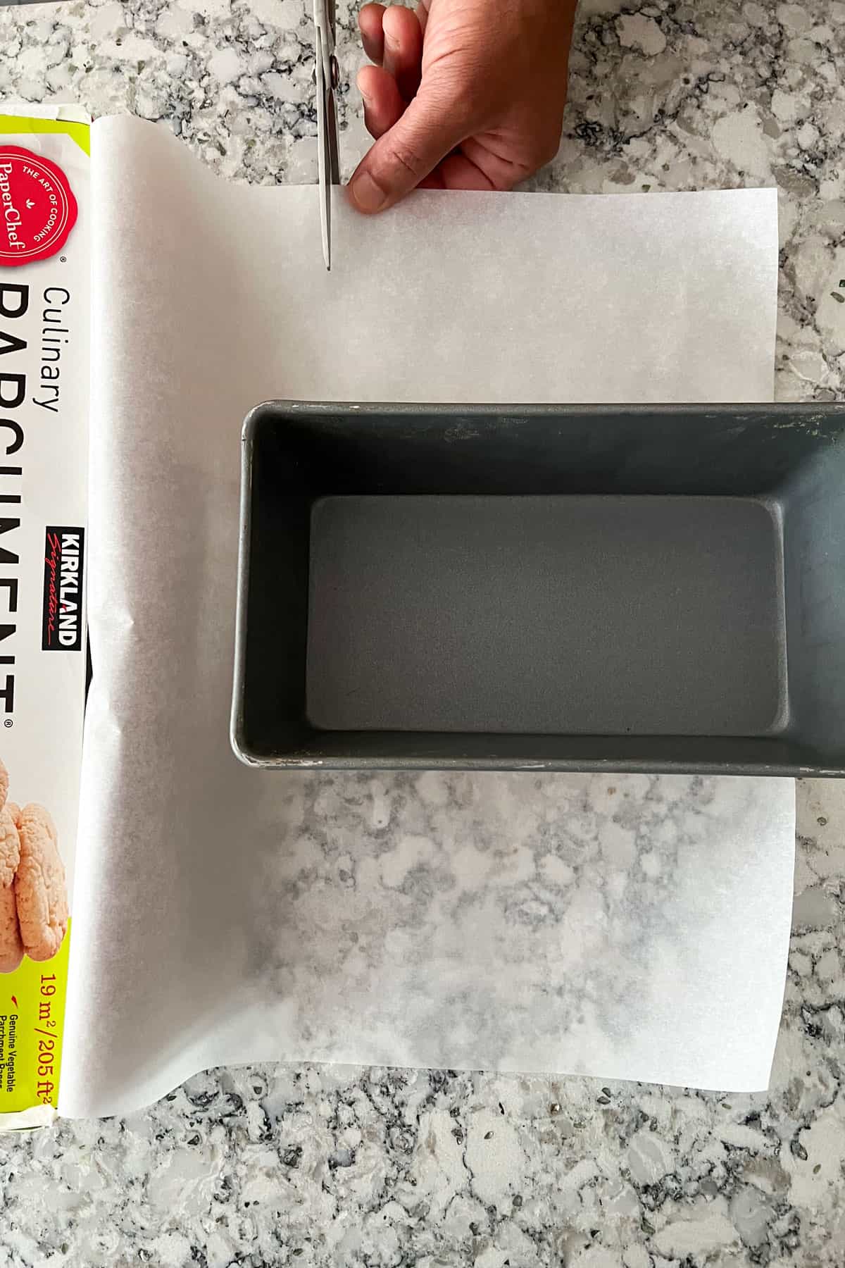loaf pan sitting on a piece of parchment paper with a scissor about to cut across it