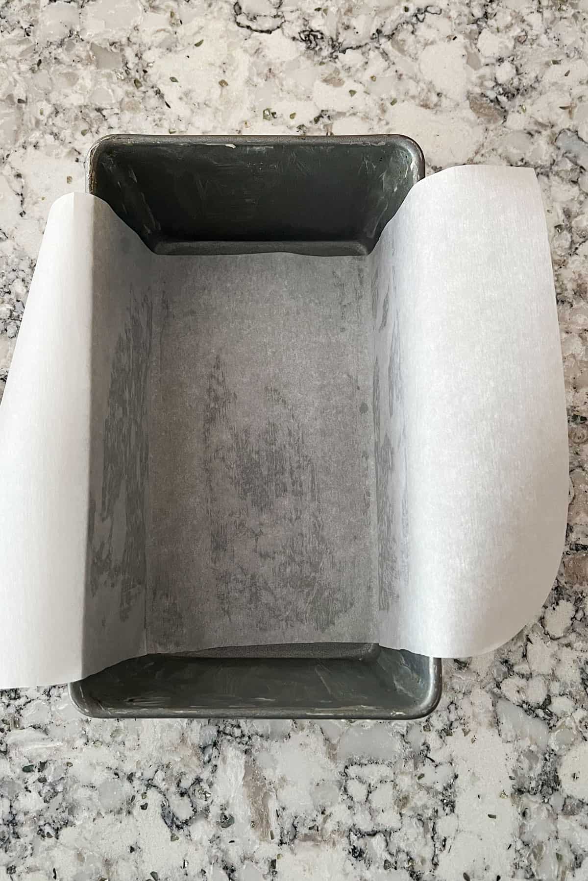 loaf pan line with parchment paper, the edges hanging over the sides of the pan.