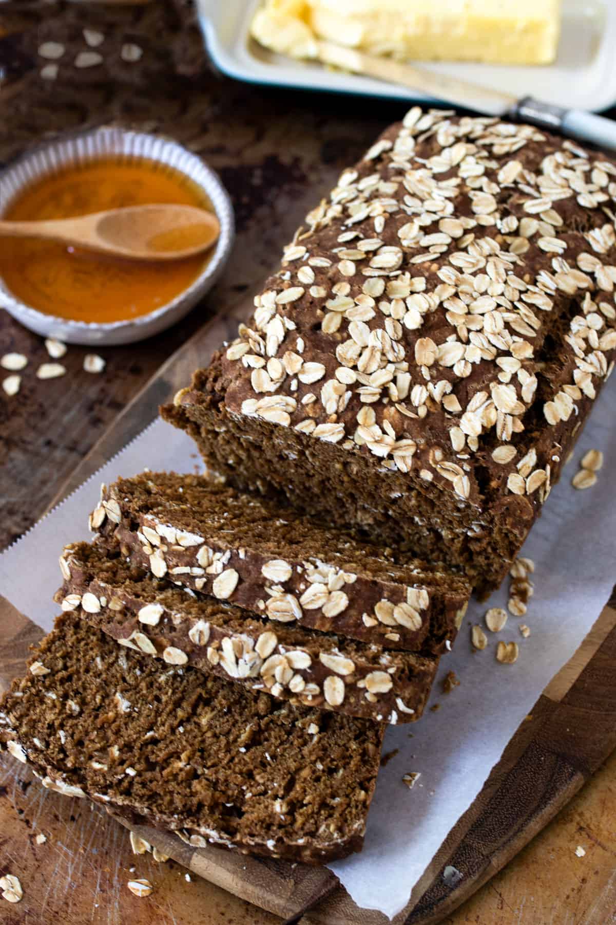 Loaf of brown bread with three slices sliced, a small bowl of honey next to it.