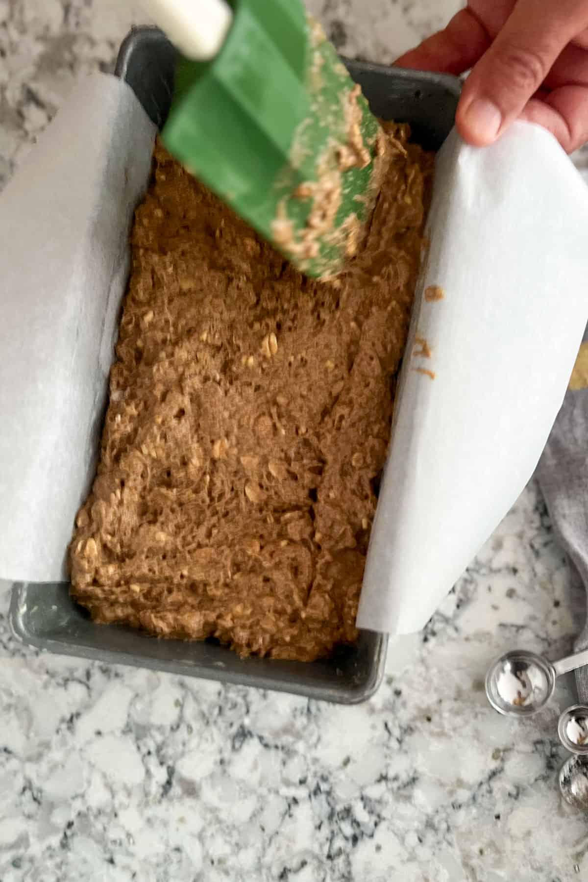 spatula smoothing brown dough into parchment lined loaf pan