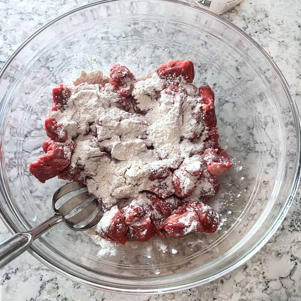 Cubes of beef in a glass bowl sprinkled with flour