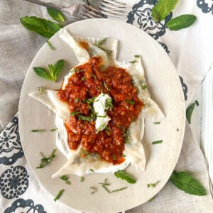 Tender looking dumplings on a bed of yogurt topped with tomato meat sauce and chopped mint.