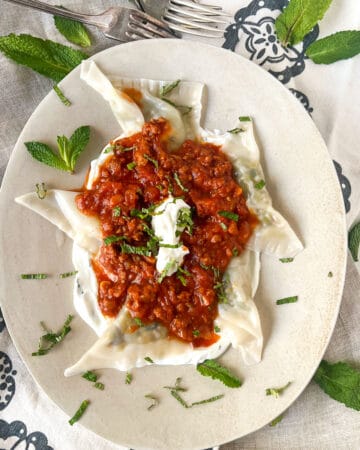 Tender looking dumplings on a bed of yogurt topped with tomato meat sauce and chopped mint.