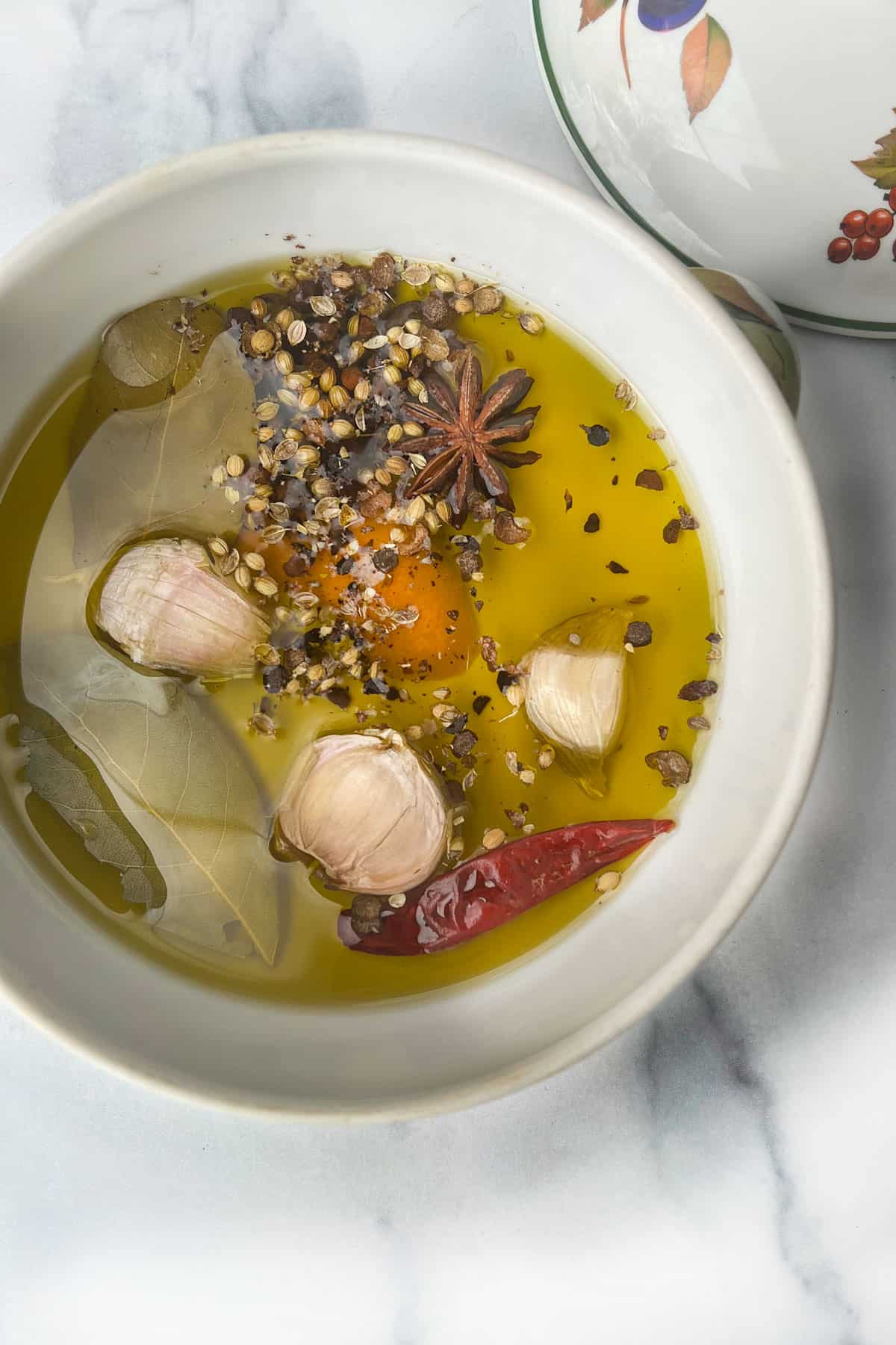 Whole spices in a small porcelain crock: garlic cloves, pepper corns, bay leaves, star anise and a dried red pepper.