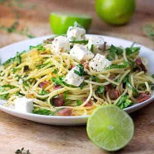 pasta with prosciutto, arugula and cubes of feta on a plate, surround with limes.