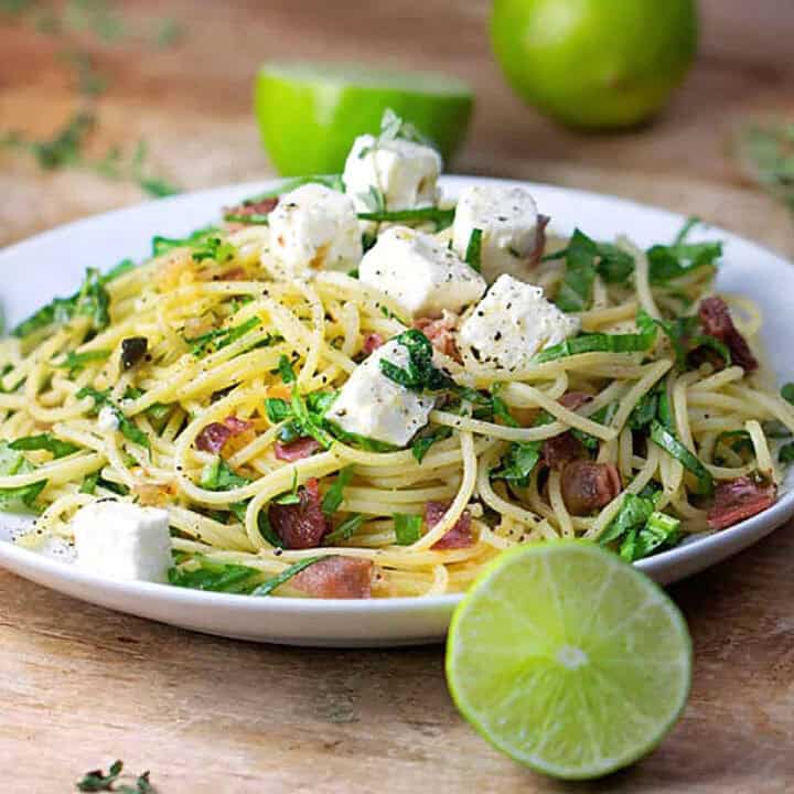 pasta with prosciutto, arugula and cubes of feta on a plate, surround with limes.