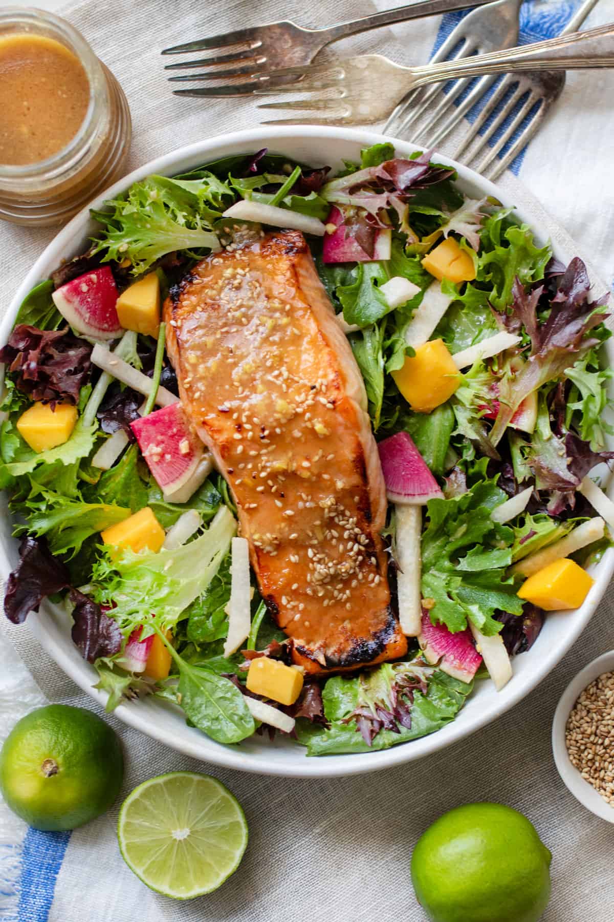 A broiled miso salmon fillet topped with miso dressing and sesame seeds on a bed of salad greens with jicama matchsticks, mango chunks and sliced watermelon radishes.