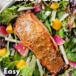 A broiled miso salmon fillet topped with miso dressing and sesame seeds on a bed of salad greens with jicama matchsticks, mango chunks and sliced watermelon radishes.