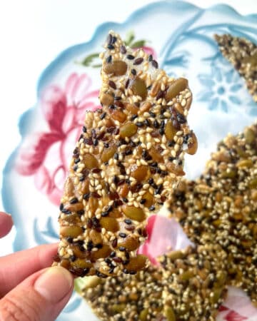 Fingers holding a thin seeded cracker.