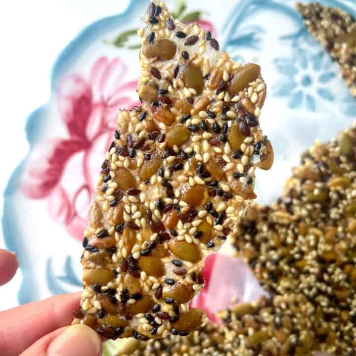 Fingers holding a thin seeded cracker.