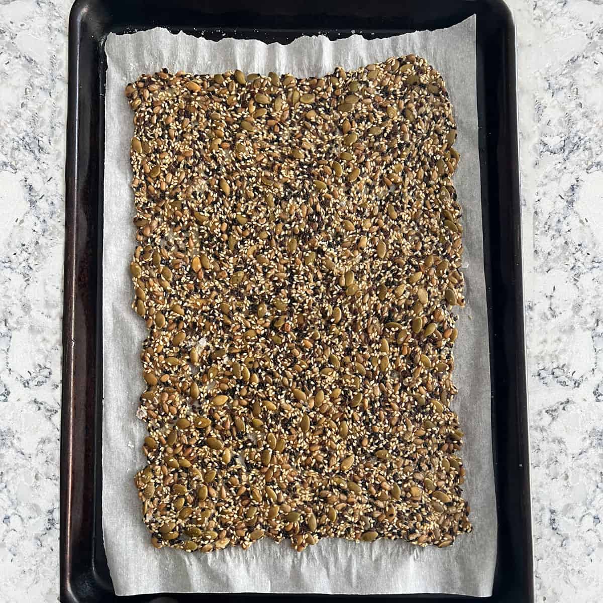 a solid sheet of seed crackers baked and golden brown on a parchment lined rimmed baking sheet.