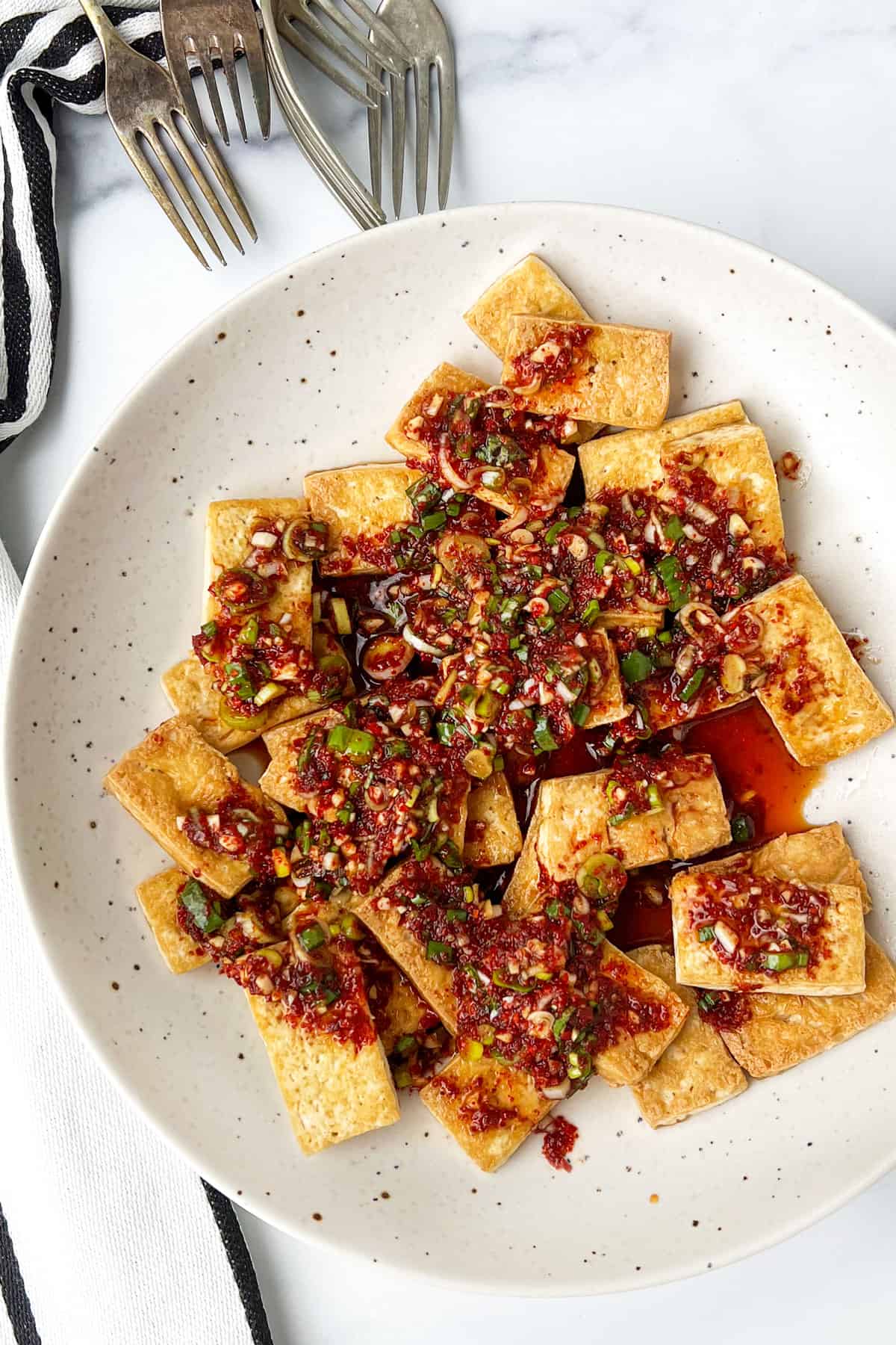 Plate topped with bite sized golden brown pieces of pan fried tofu, topped with a richly textured sauce with Korean pepper flakes and scallions.