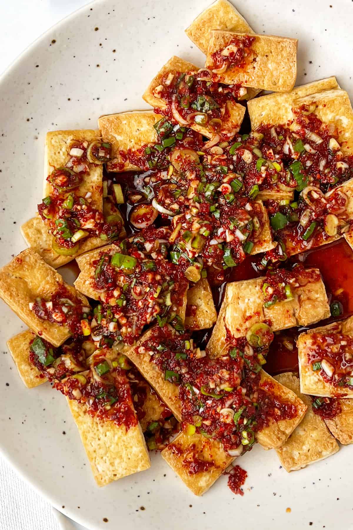 bite sized pieces of golden brown tofu on a plate, topped with thick sauce.