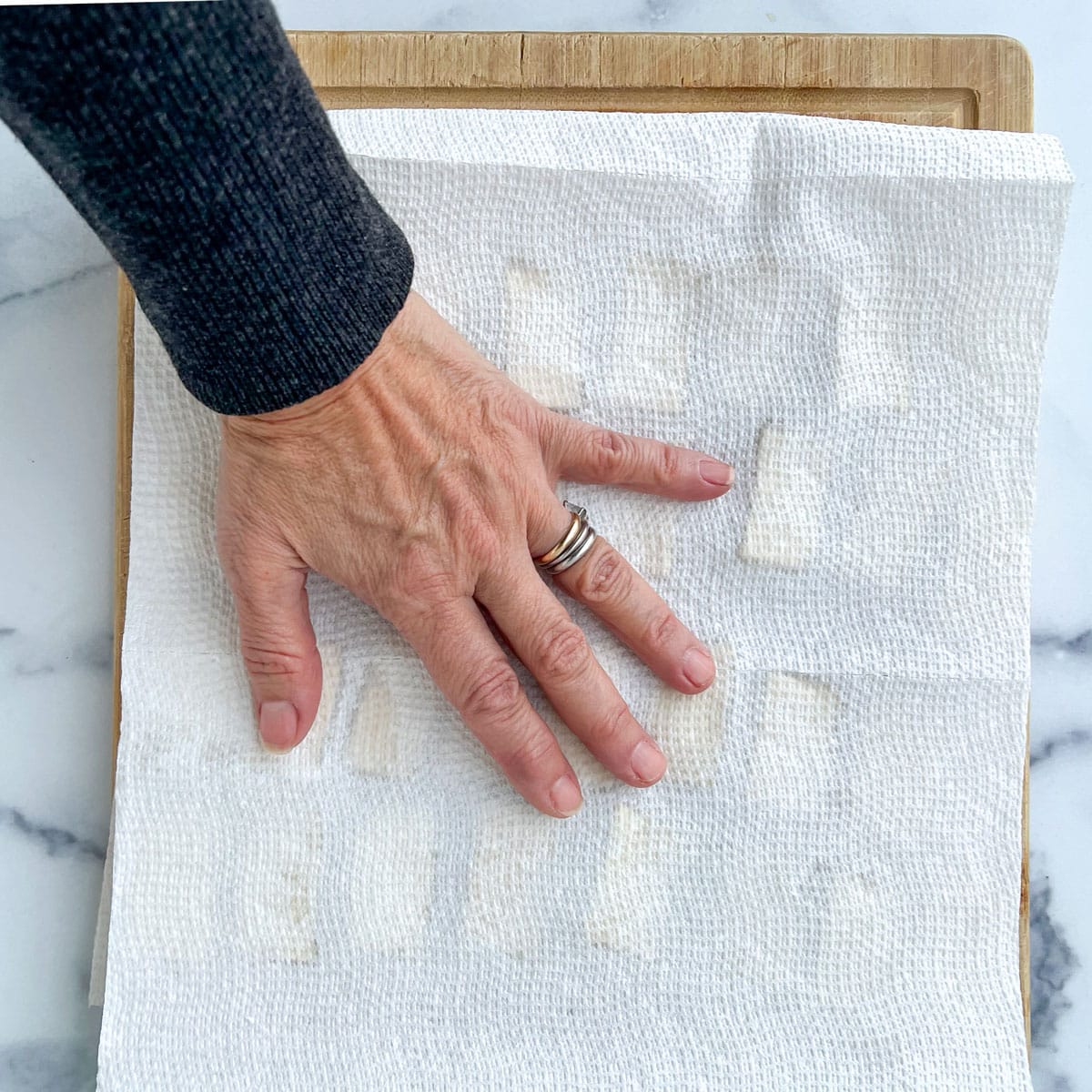 small rectangular pieces of tofu showing through a damp paper towel with a hand pressing down on it.