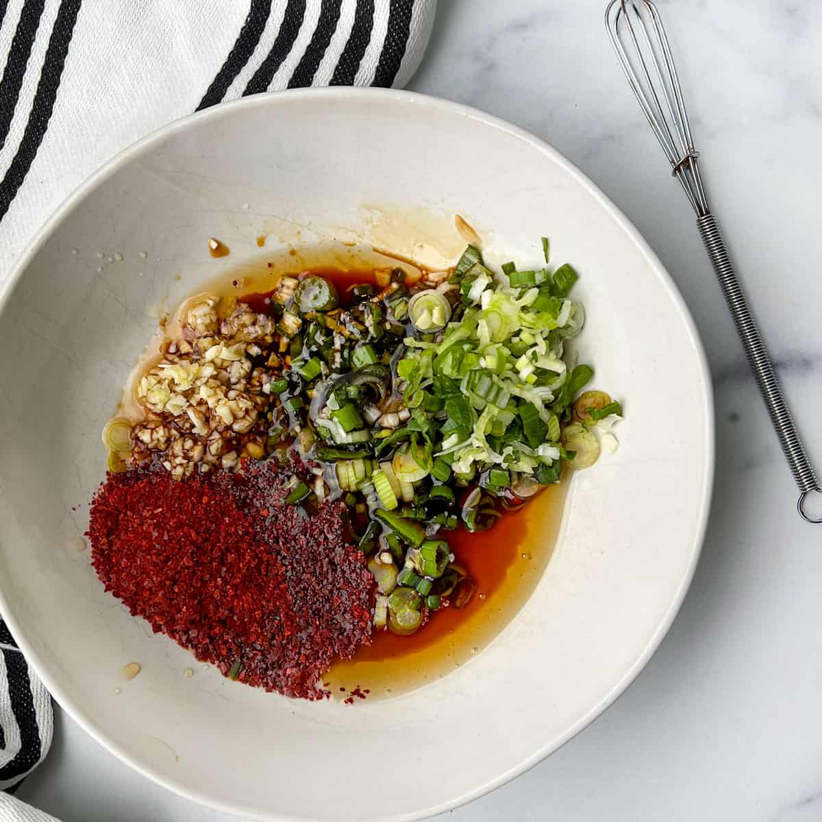 Ingredients added to a small white bowl, chili flakes, chopped scallions, minced garlic, oil and soy sauce.