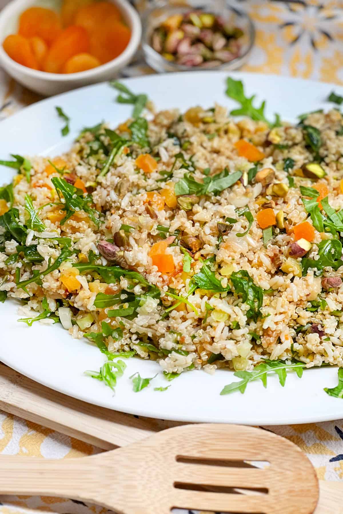 platter of rice and quinoa salad with a small bowl of dried apricots and a small bowl of toasted pistachio nuts in the background.