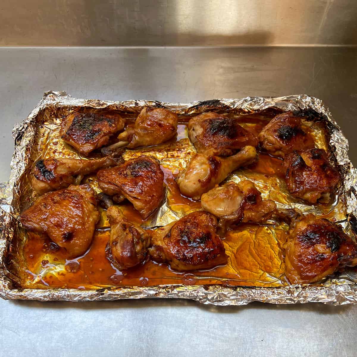 A dozen or so pieces of  deep golden brown and saucy baked apricot chicken pieces on a foil lined baking sheet.