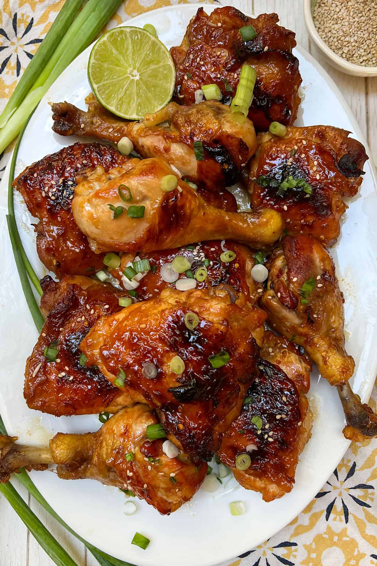 golden brown baked apricot chicken thighs and drumsticks on an oval platter topped with chopped scallions and sesame seeds.