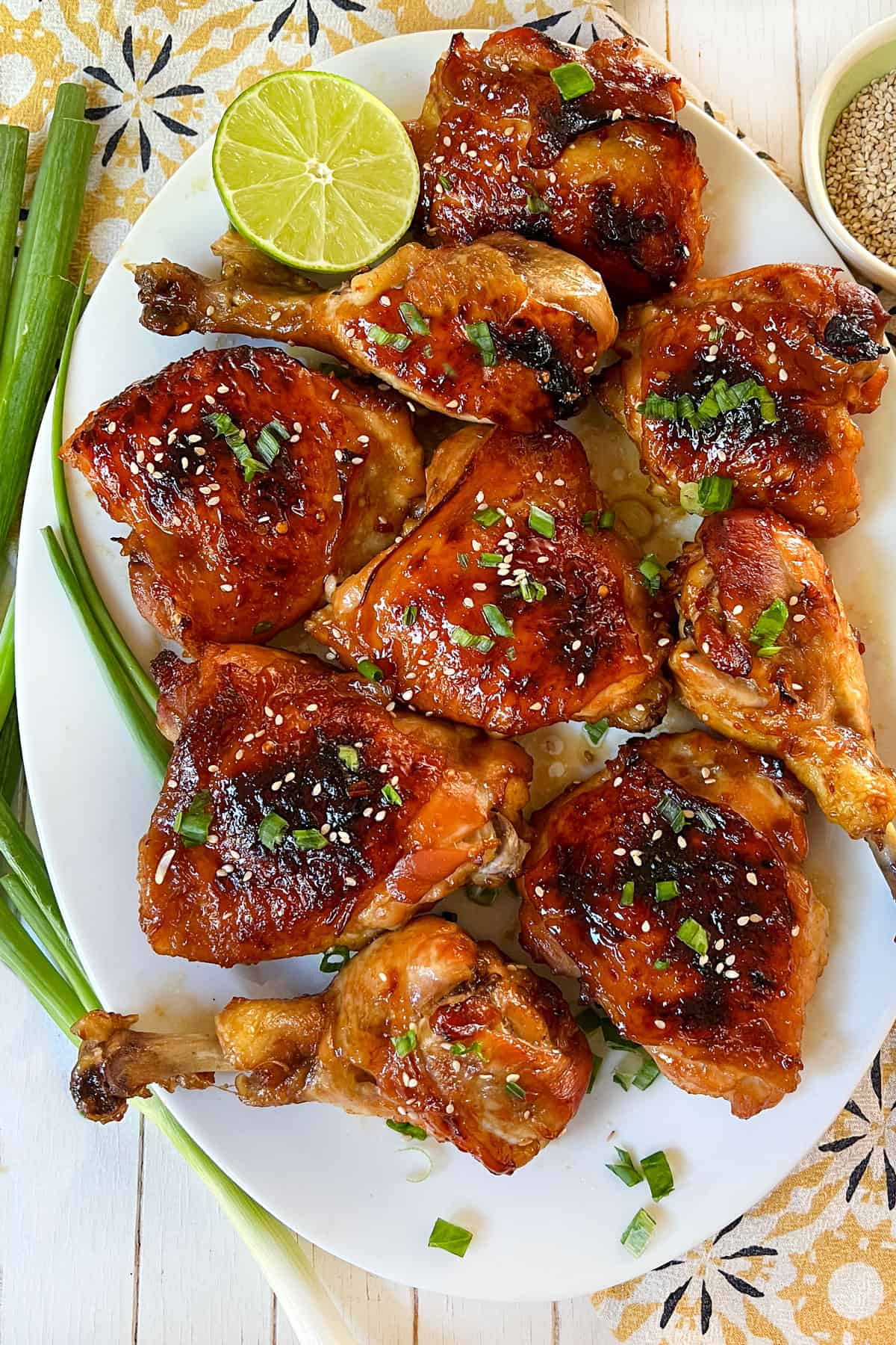 golden brown baked apricot chicken thighs and drumsticks on an oval platter topped with chopped scallions and sesame seeds.