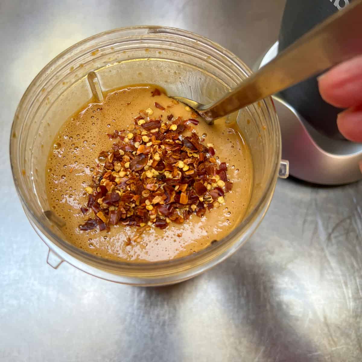 crushed red pepper flakes being stirred into apricot glaze mixture in the cup of a small food processor.