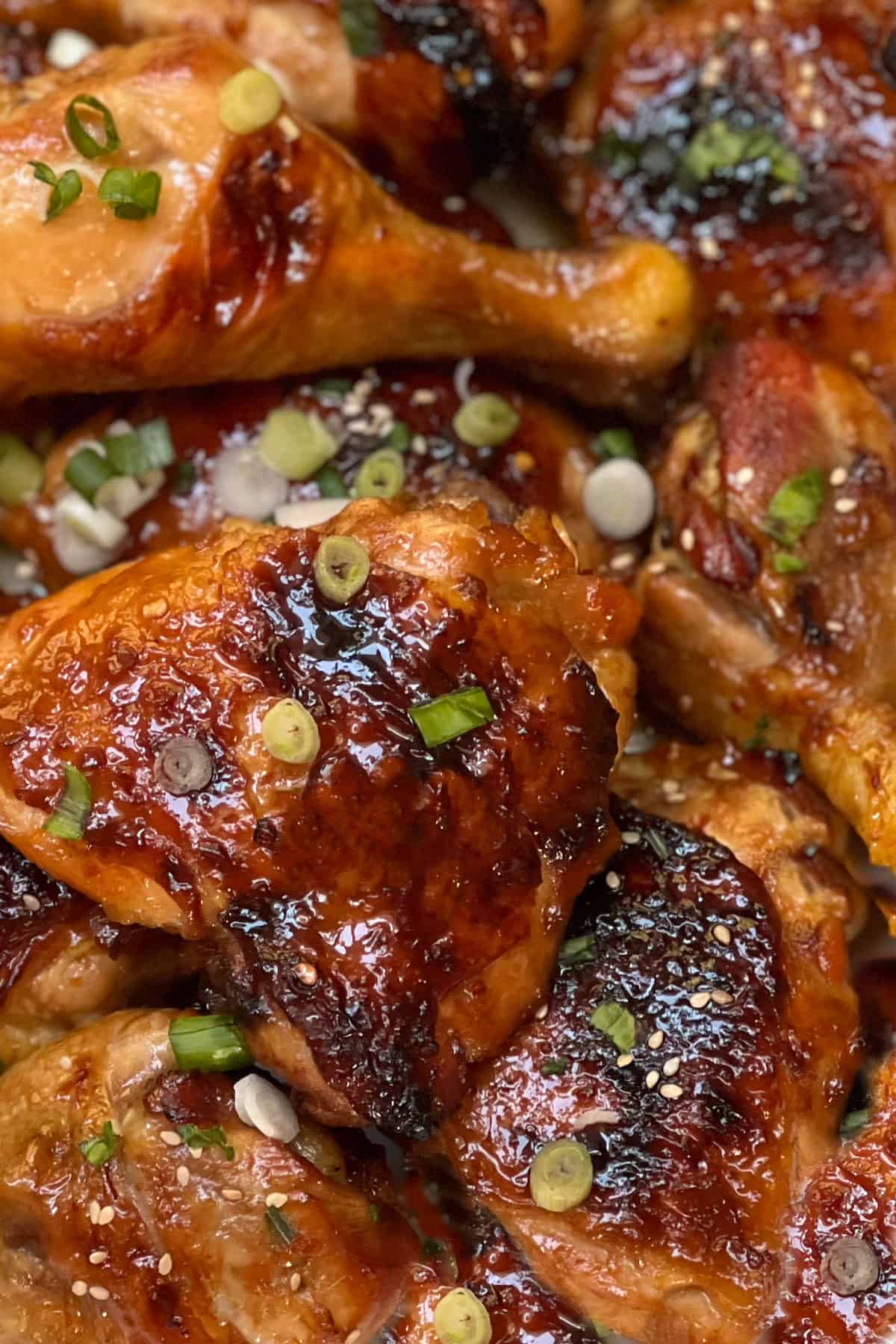 a piece of golden brown apricot chicken thigh topped with chopped scallions and surrounded with sauce.