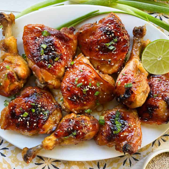 8 pieces of baked apricot chicken on a platter, topped with chopped scallions.