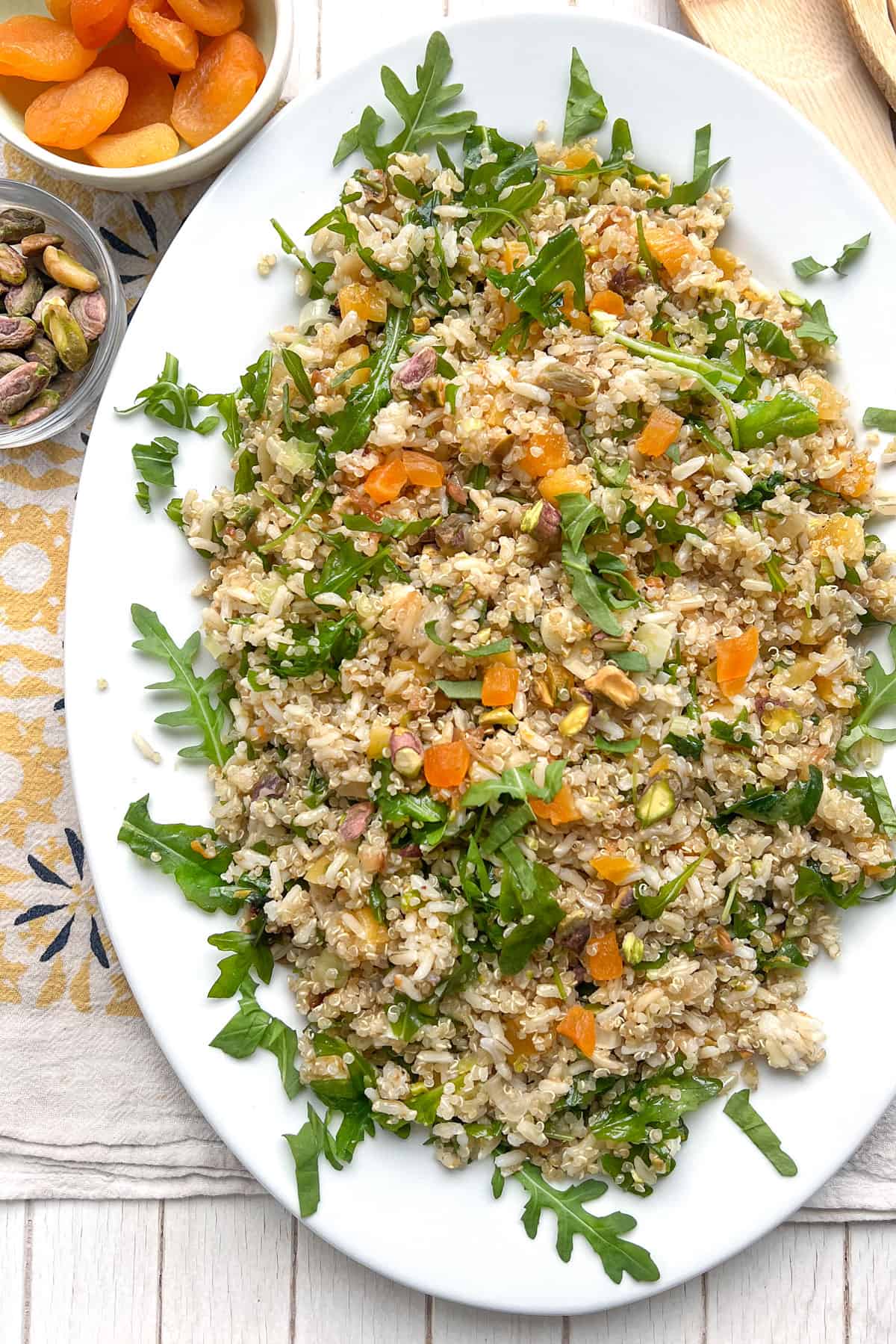 Oval platter topped with rice and quinoa salad with chopped apricots, pistachios and arugula.