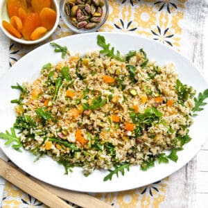 platter of rice and quinoa salad with a small bowl of dried apricots and a small bowl of toasted pistachio nuts in the background.