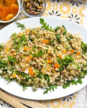 platter of rice and quinoa salad with a small bowl of dried apricots and a small bowl of toasted pistachio nuts in the background.