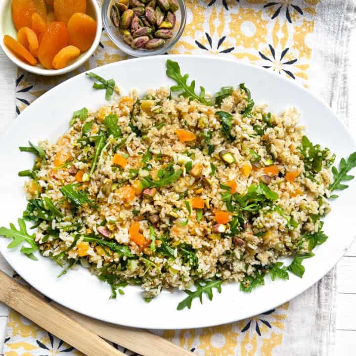 platter of rice and quinoa salad with a small bowl of dried apricots and a small bowl of toasted pistachio nuts in the background.
