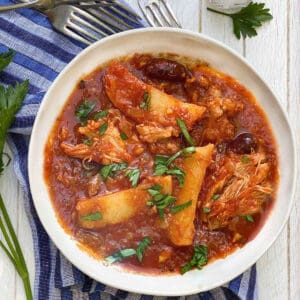 Greek chicken stew with potatoes and olives in a bowl with chopped parsley sprinkled on top