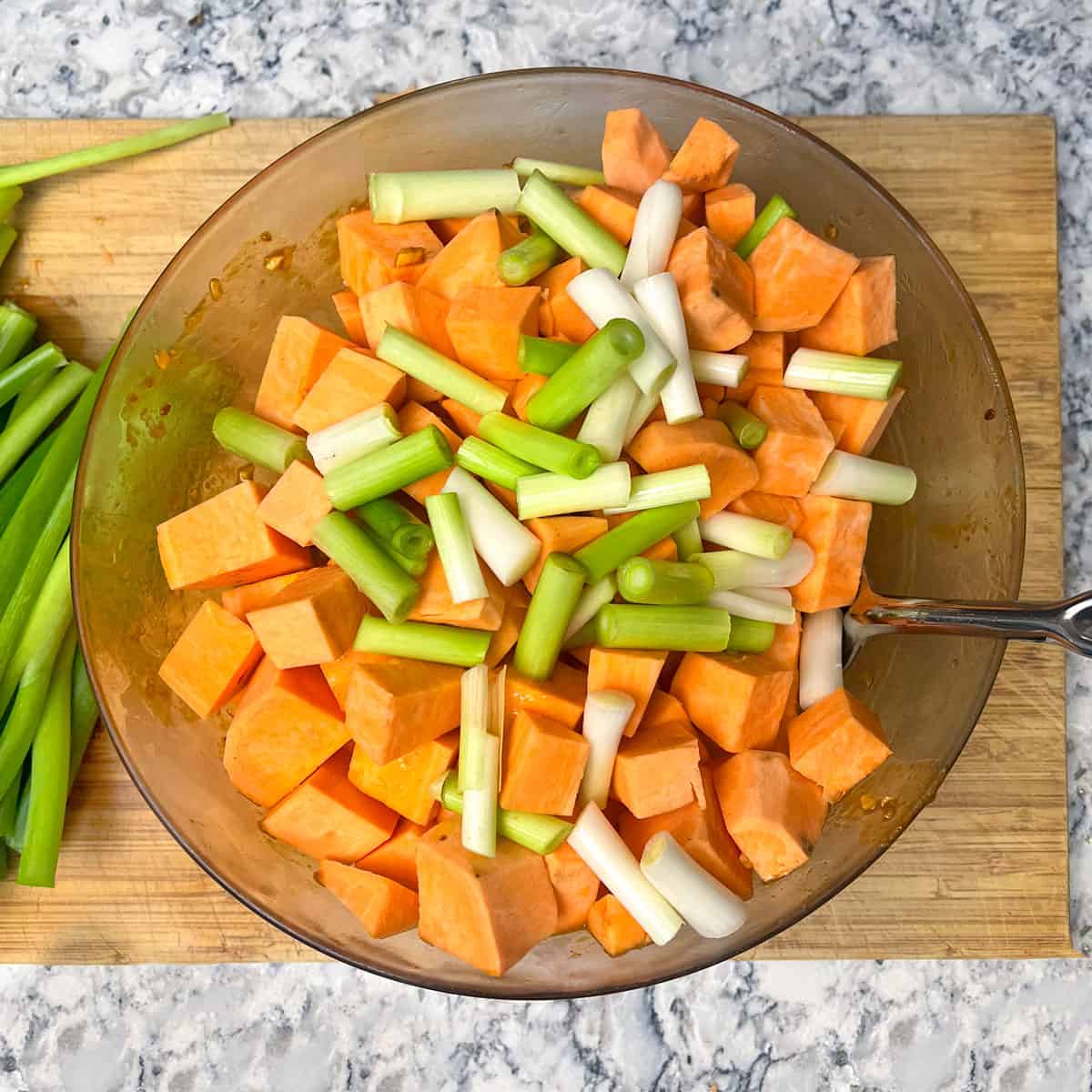Cubes of raw sweet potatoes and 1-inch segments of scallions tossed together in a glass mixing bowl