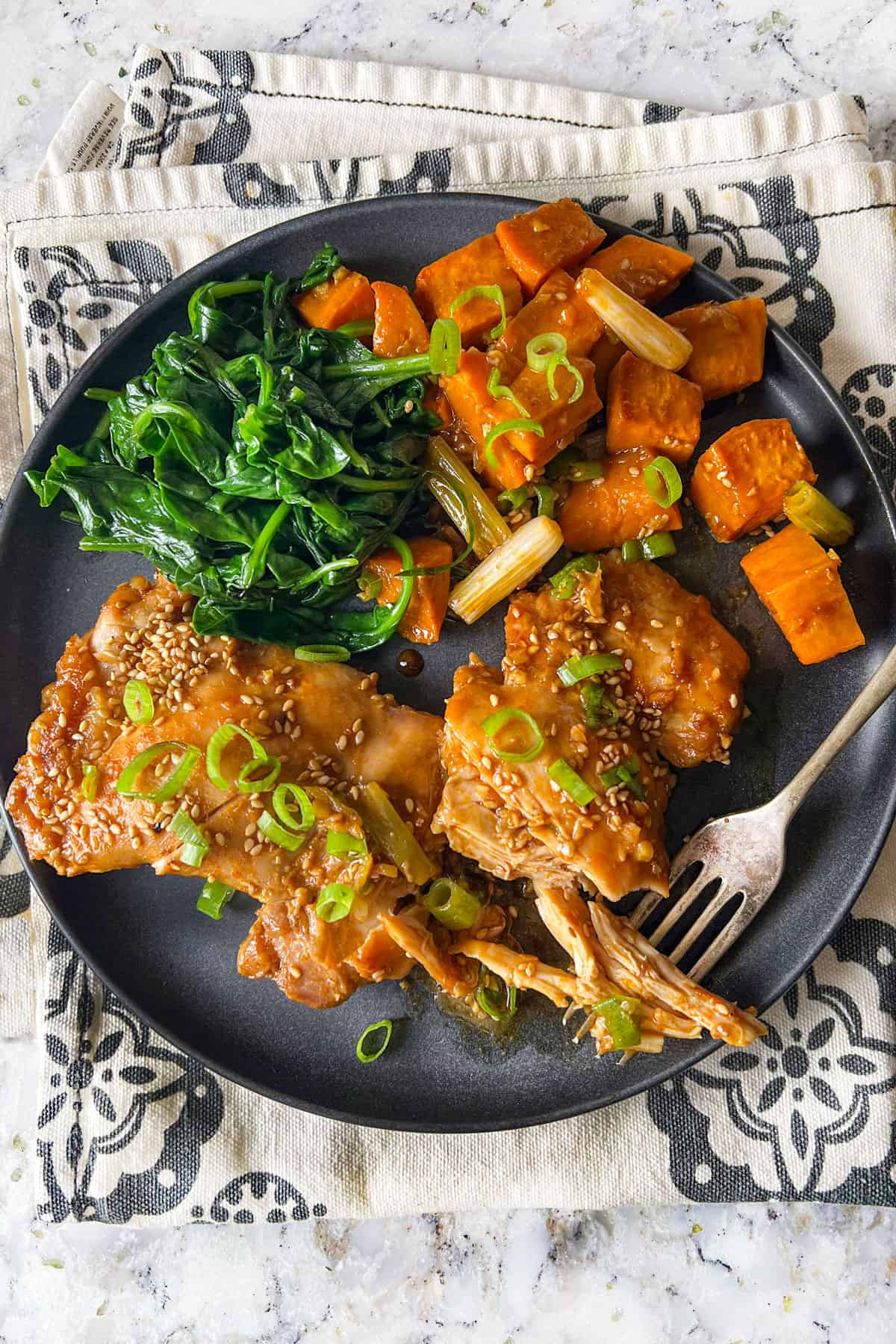 two baked chicken thighs with roasted sweet potato cubes and sauteed spinach on a plate.