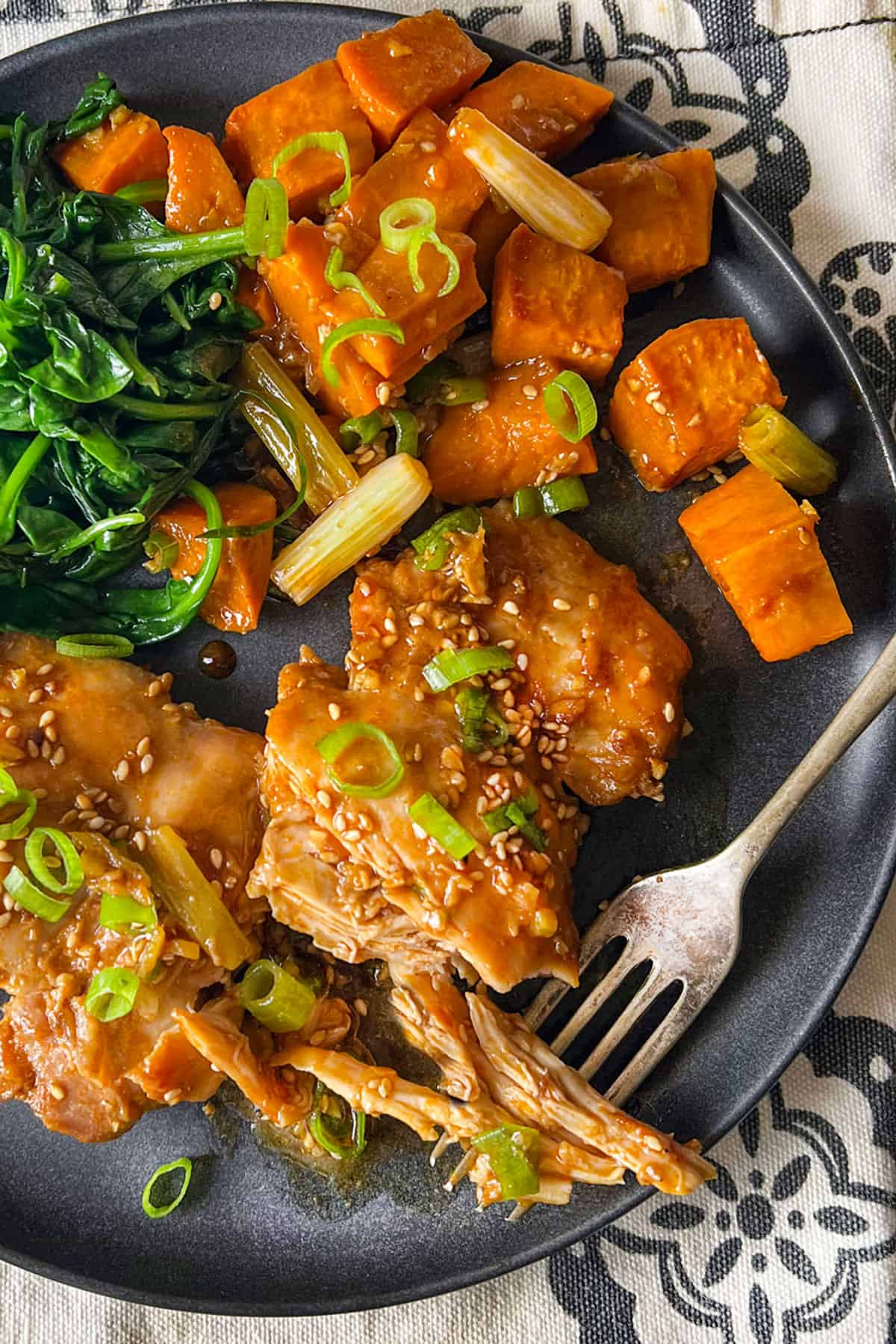 two baked chicken thighs with roasted sweet potato cubes and sauteed spinach on a plate.