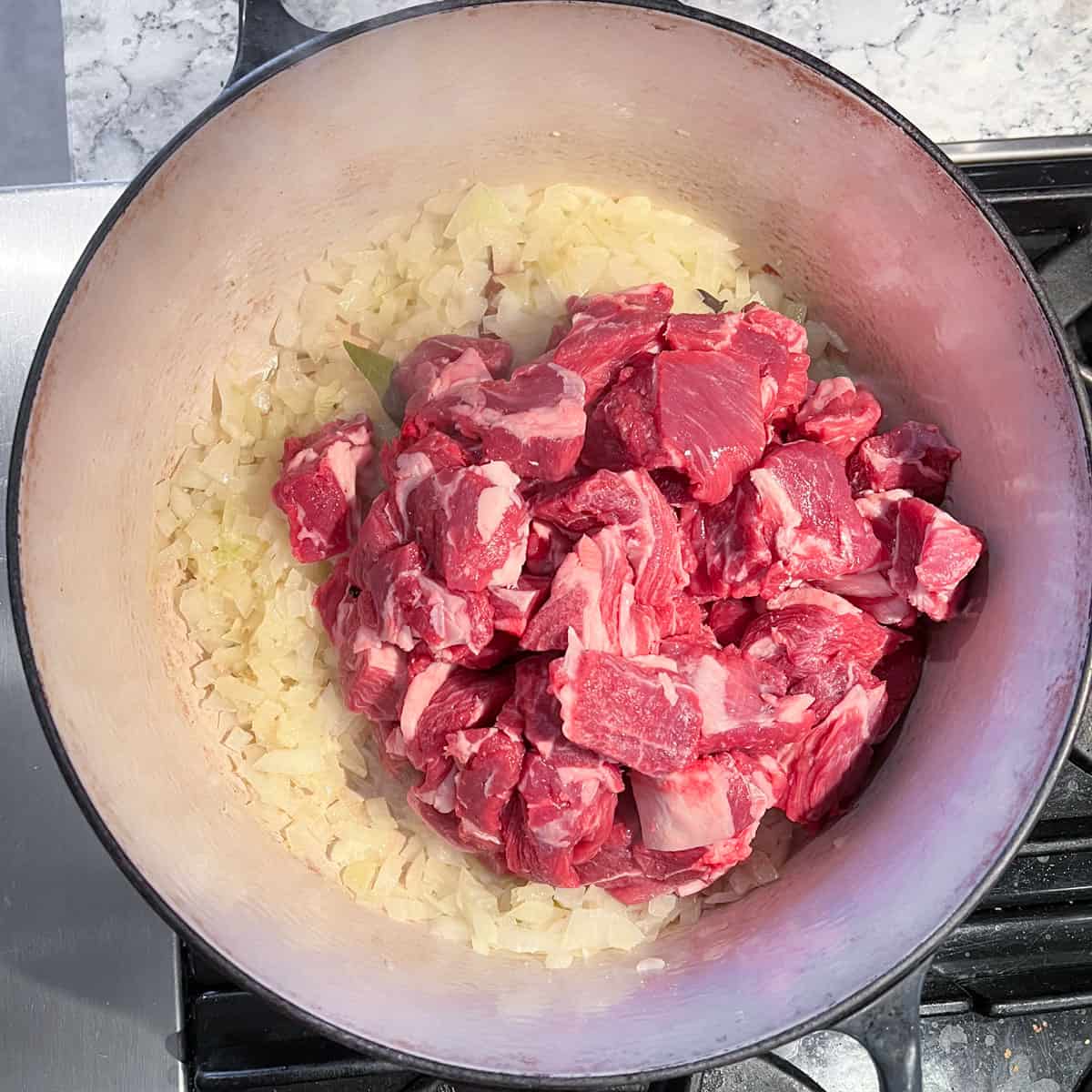 Dutch oven with raw cubes of lamb on top of sautéd onions.