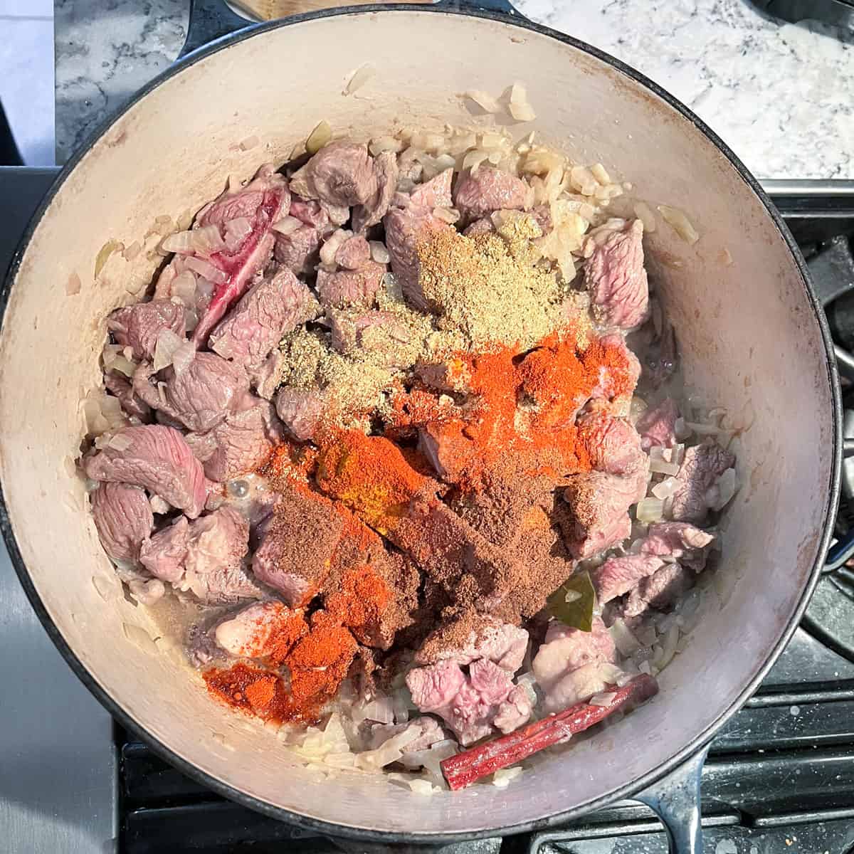 Dutch oven with browned lamb cubes topped with colorful spice for lamb rogan josh.