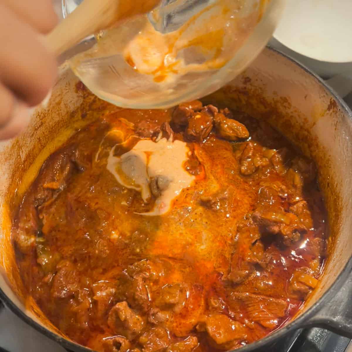 Adding yogurt to a pot of rogan josh when it is almost done cooking.