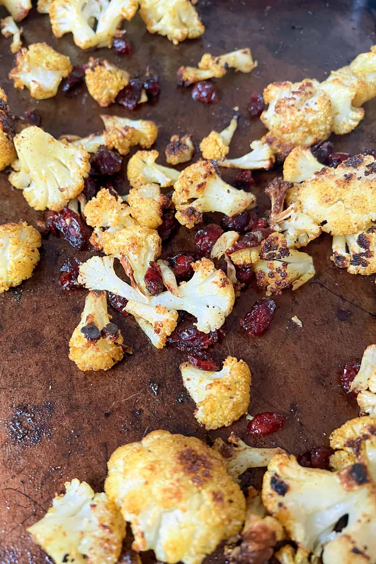 curried roasted cauliflower florets on a sheet pan tossed with dried cranberries.