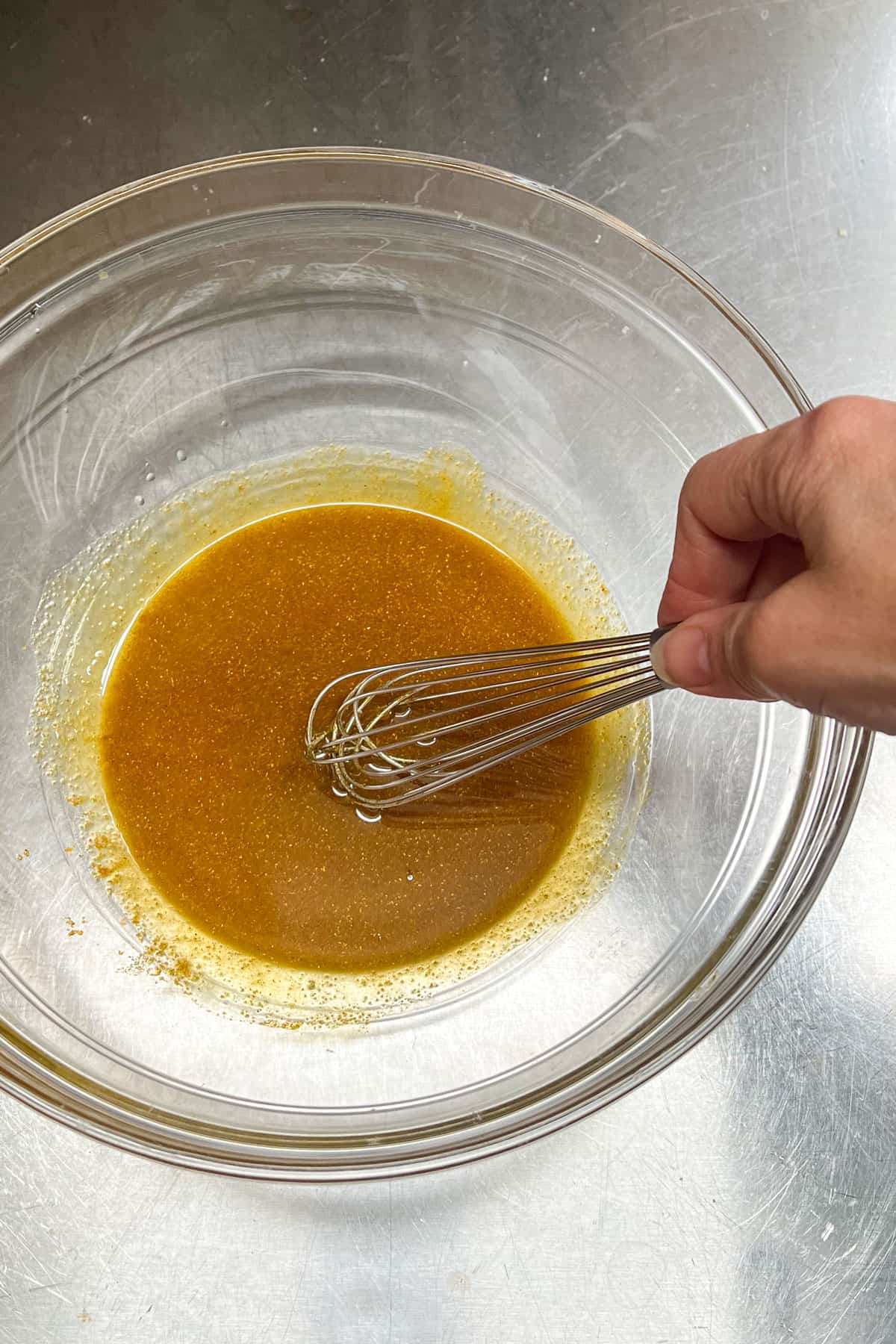 Whisking olive oil and curry powder in a large glass mixing bowl to make roasted curried cauliflower.