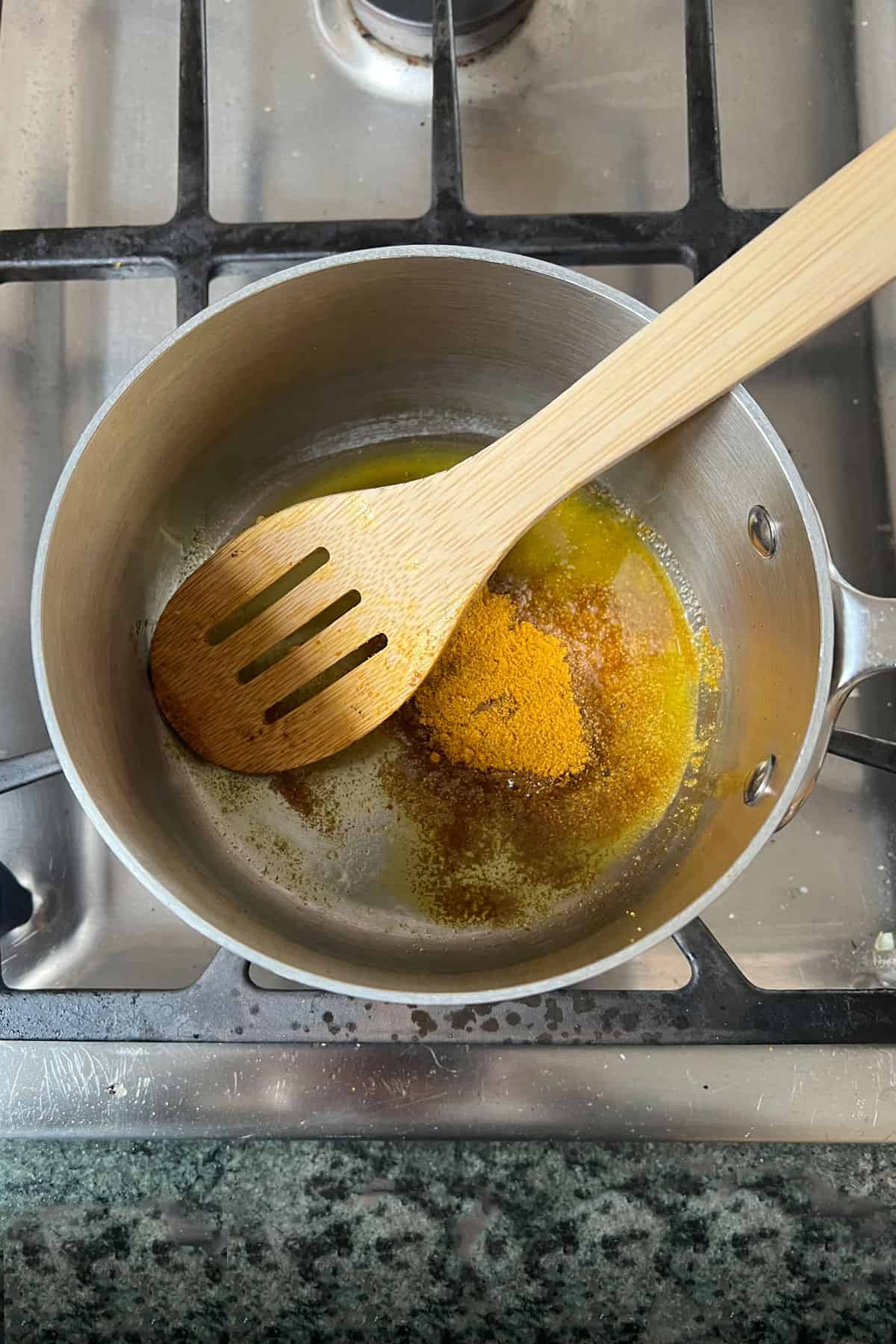 Olive oil and curry powder in a small sauce pan being stirred with a wooden spoon.