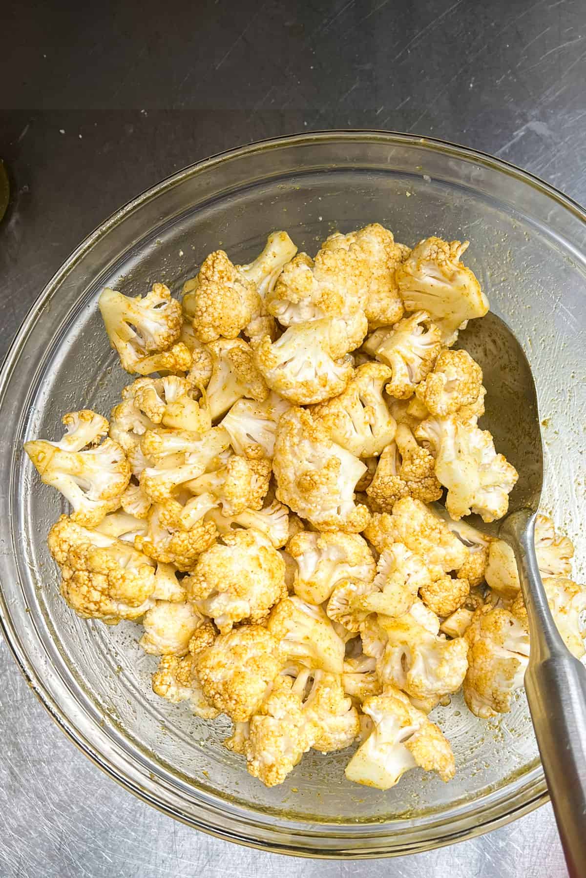 Cauliflower florets tossed with oil and curry powder, in a large mixing bow.