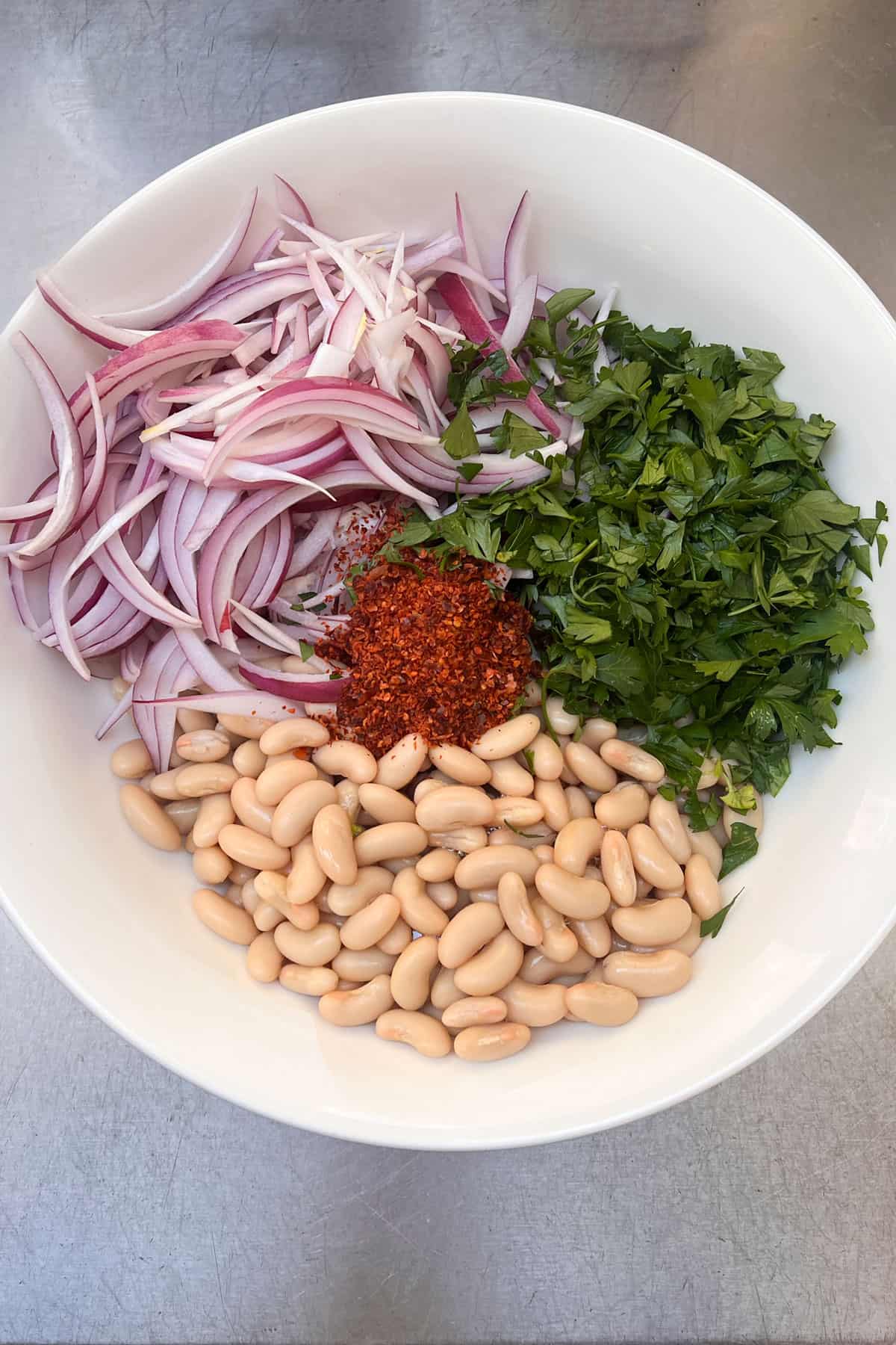 ingredients for Turkish white bean salad in a bowl: white beans, chopped parsley, sliced red onions and Aleppo pepper.