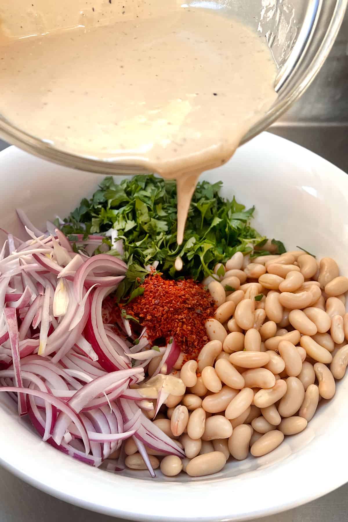 pouring tahini dressing on Turkish white bean salad in a bowl.
