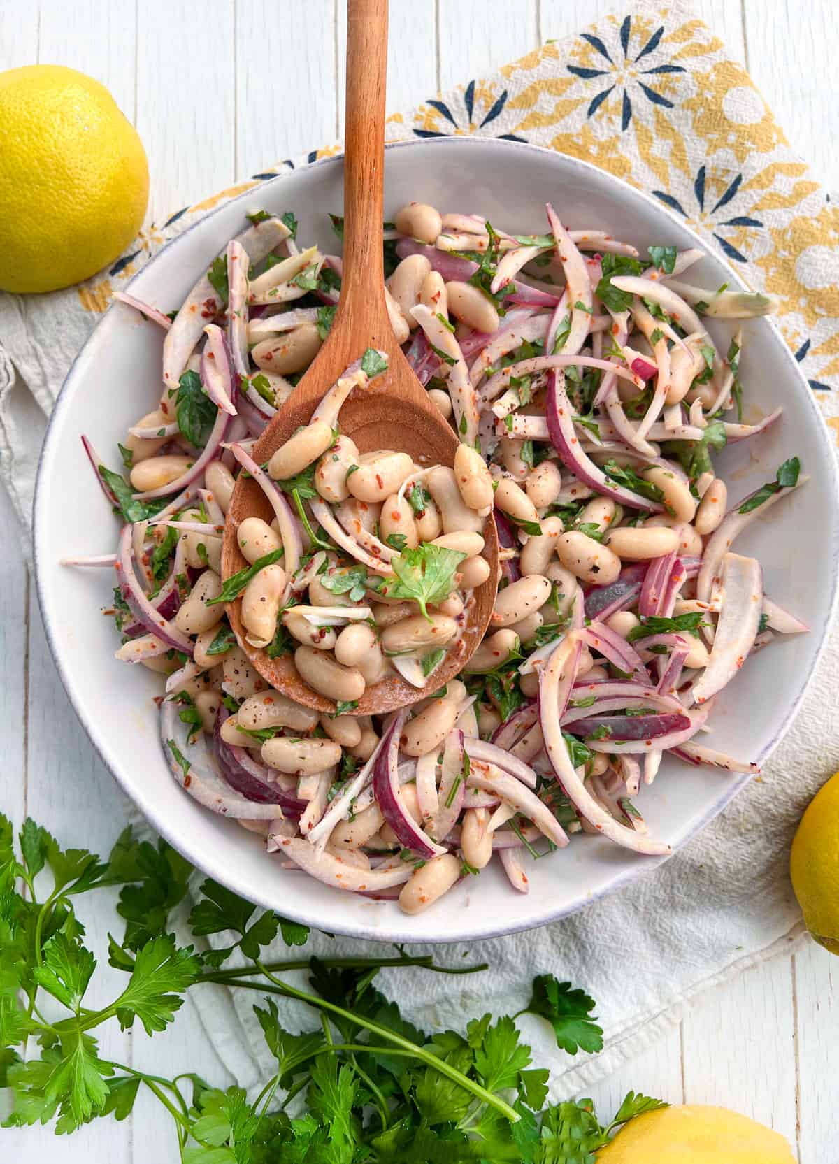 white bean salad with onions and parsley in a serving bowl with a wooden spoon