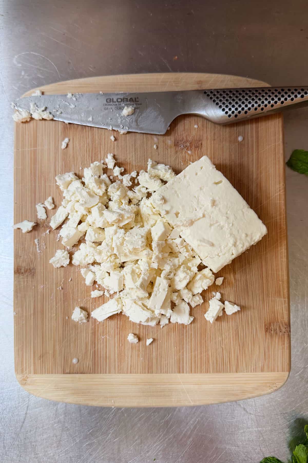 A block of sheepsmilk feta on a cutting board, half of it chopped into crumbles.