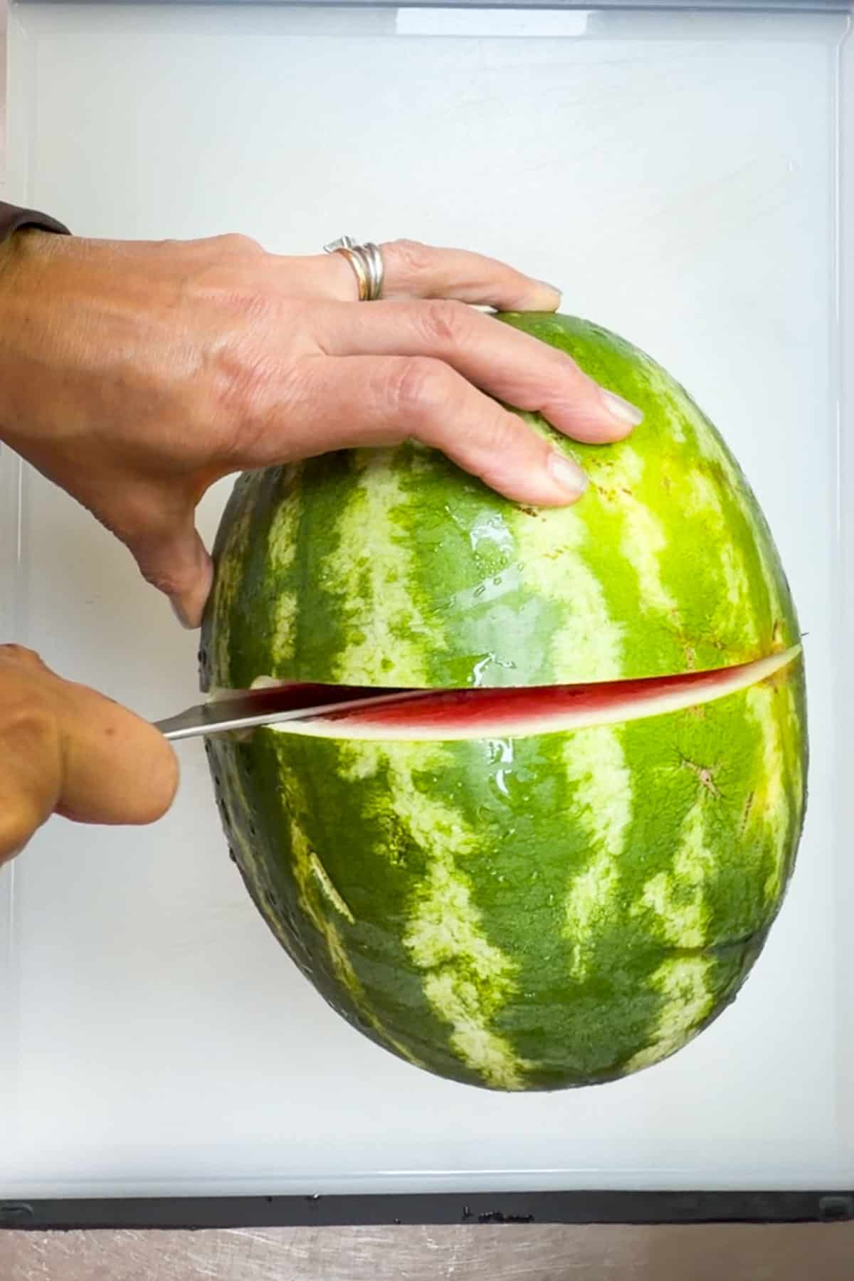 cutting a watermelon in half on a cutting board
