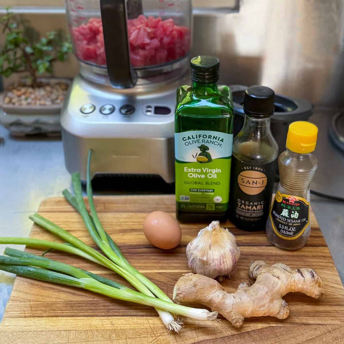 Ingredients for Ahi tuna burgers on a kitchen counter: diced ahi tuna in a food processor, scallions, ginger, garlic, soy sauce, sesame oil, olive oil and an egg.