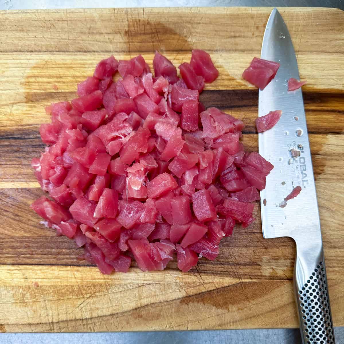 Diced Ahi tuna steak on a wooden cutting board.