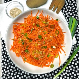 Ginger carrot slaw in a serving bowl topped with chopped scallions and sesame seeds.